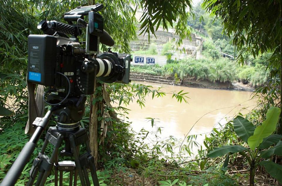 câmara de filmagem aponta para a outra margem de um rio de cor castanha, onde se vêem cartazes com a palavra GAP