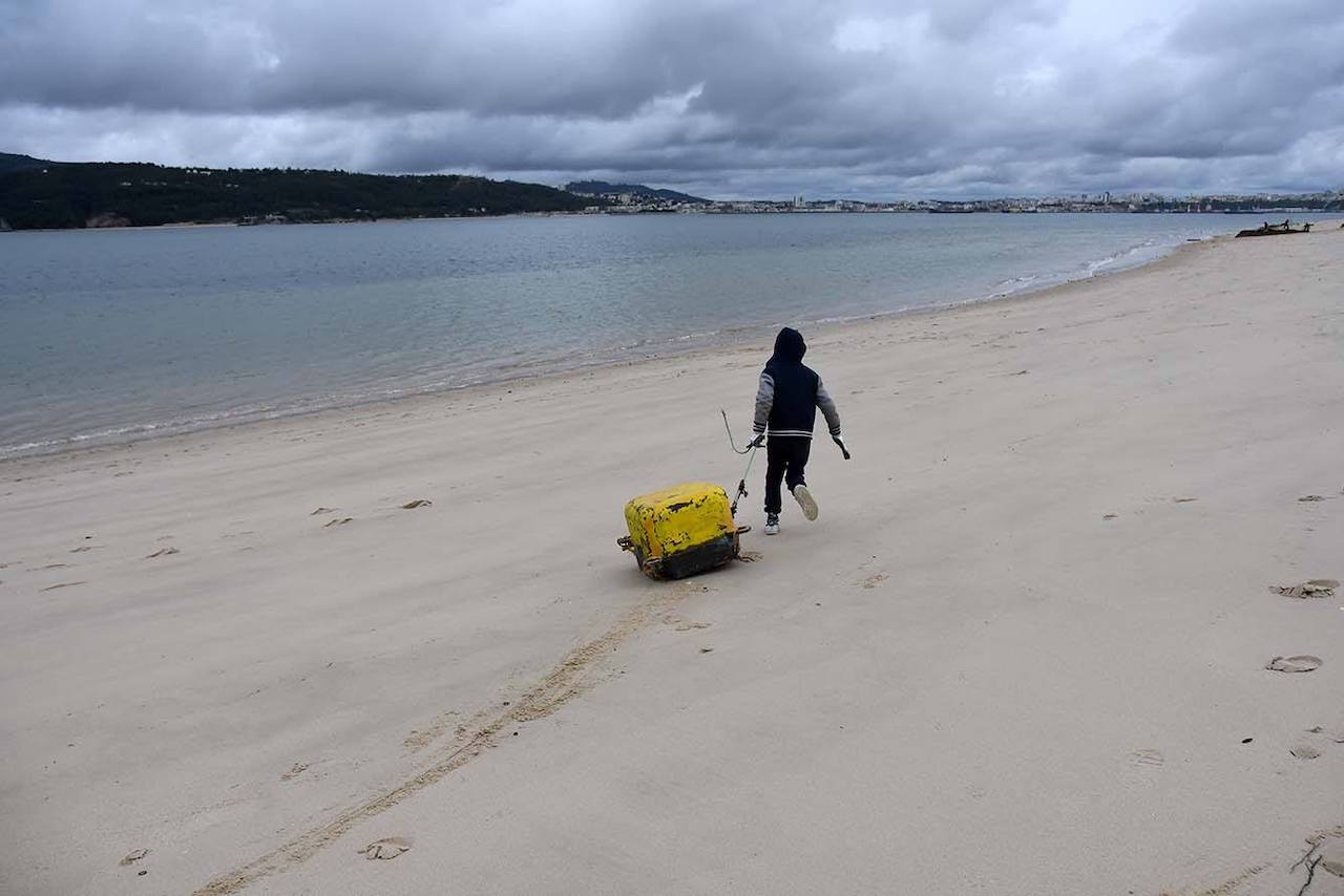 rapaz arrasta grande pedaço de lixo na areia