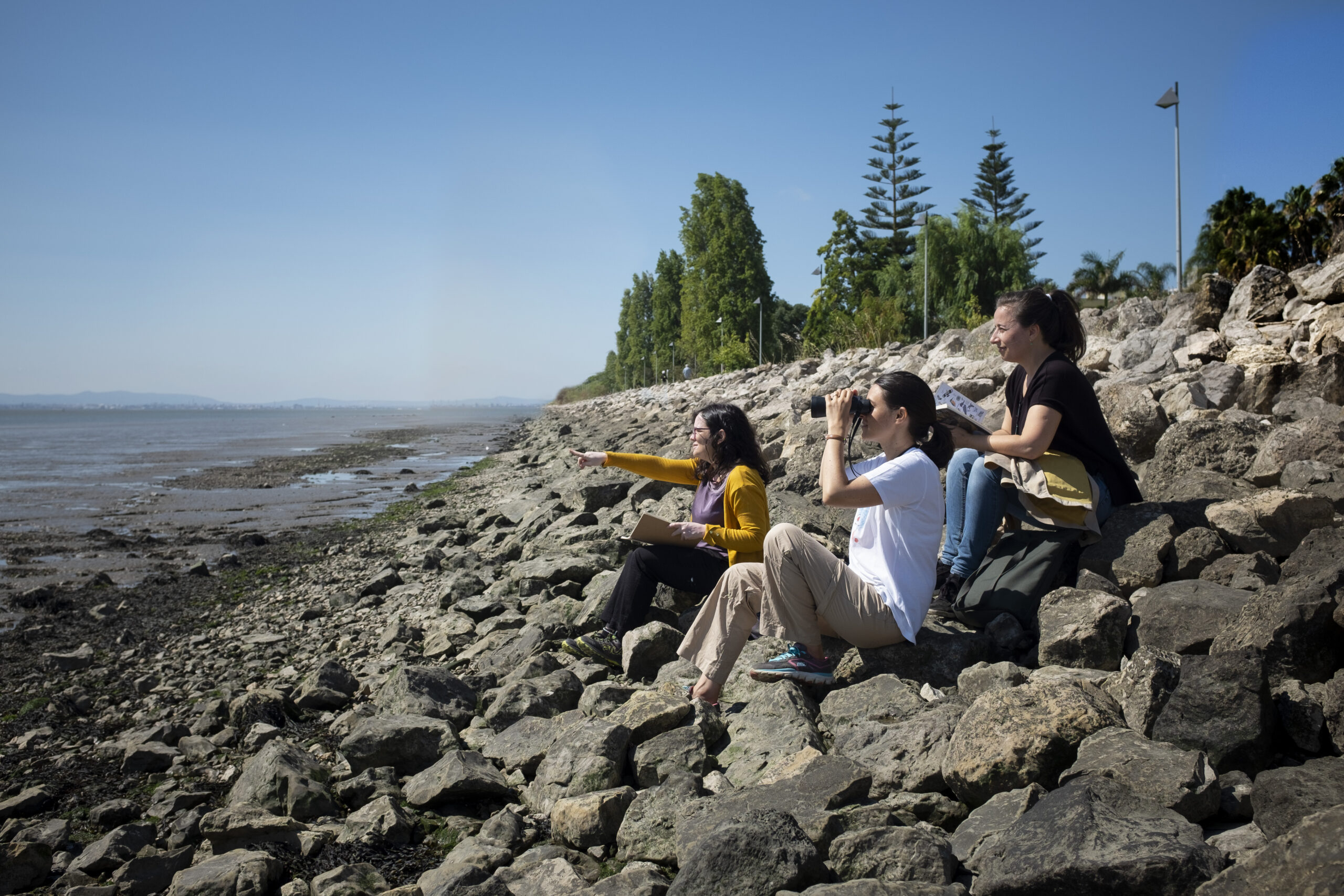 Inês Sequeira, Helena Geraldes e Joana Bourgard sentadas à margem do Tejo a observarem a Natureza